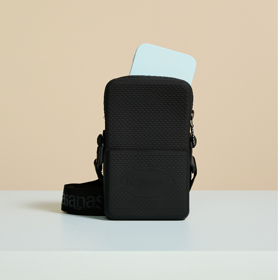 Bolsa preta Havaianas com textura e alça, segurando smartphone azul claro, ideal para passeios e viagens.