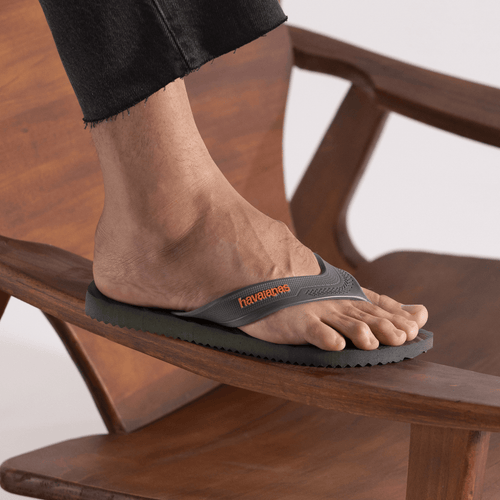 Chinelo Havaianas cinza com logo laranja, usado em pé sobre cadeira de madeira, estilo confortável e casual.