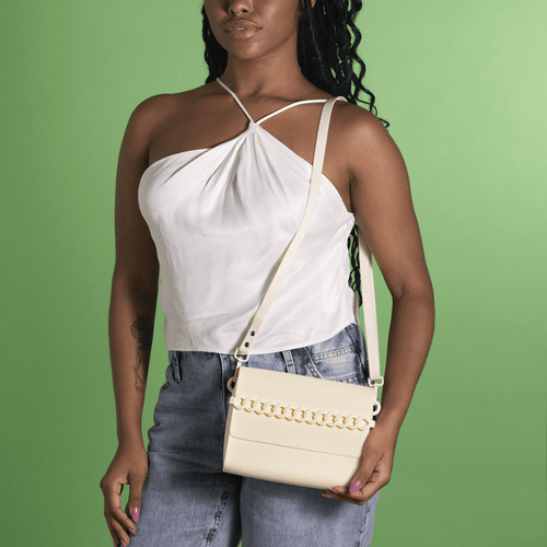 Bolsa transversal bege com corrente, usada com top branco e jeans, ideal para looks casuais e estilosos